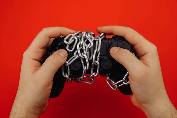 Hands of a young man holds a game controller is tied by chain isolated on red background — Stock Photo, Image