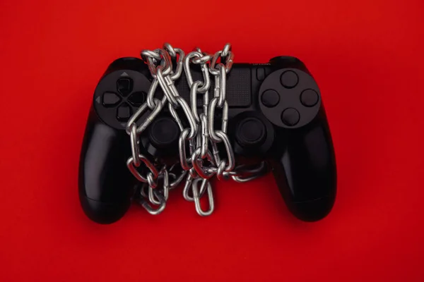 Game addiction concept. Gamepad is tied by chain isolated on red background