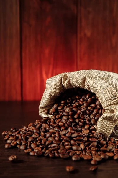 Granos de café esparcidos de la bolsa en la mesa de madera de cerca. Imagen vertical — Foto de Stock