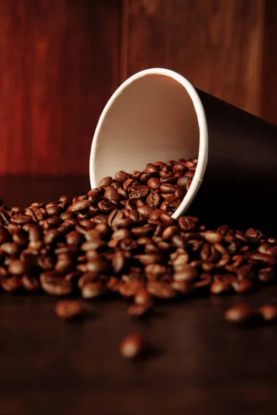 Una taza de papel de café con granos de café sobre fondo de madera. Imagen vertical — Foto de Stock