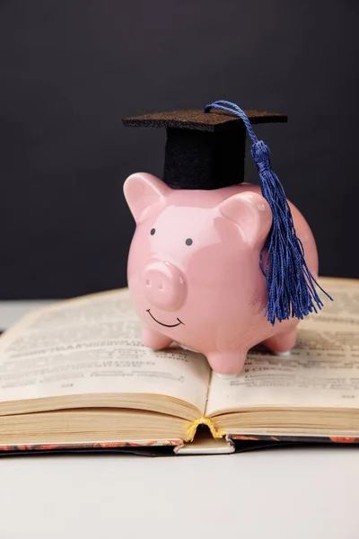 College, diploma, onderwijsconcept. Roze spaarvarken in cap blijft op het boek — Stockfoto