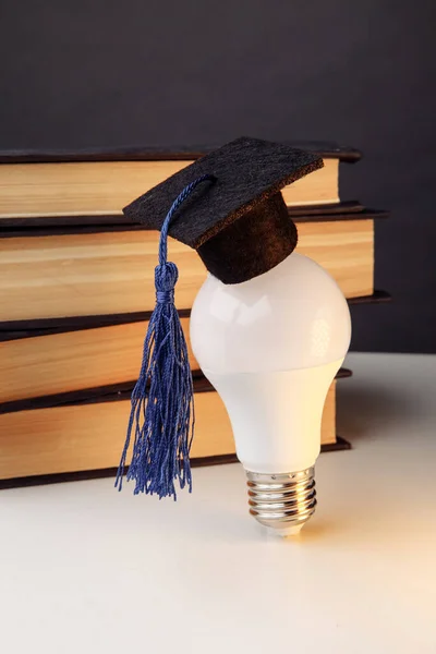 Graduation cap on light bulb with books close-up. Education idea. Vertical image — Stock Photo, Image