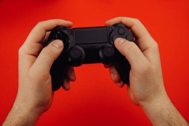 Genç adam kırmızı arkaplanda izole edilmiş bir oyun kumandası tutuyor