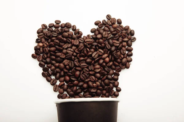 Granos de café formando corazón y taza de café sobre fondo blanco — Foto de Stock