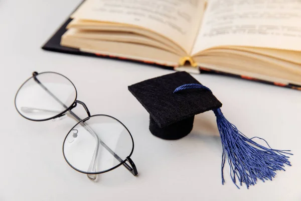 Topi kelulusan dan kacamata dengan buku terbuka close-up. Konsep pendidikan — Stok Foto