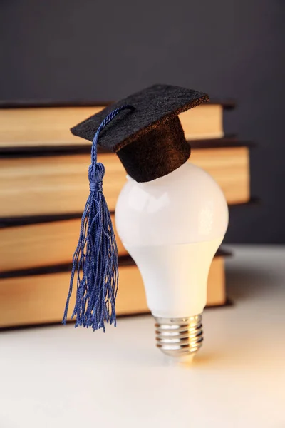 Graduation hat on light bulb with books on a table. Vertical image. Education concept — Stock Photo, Image