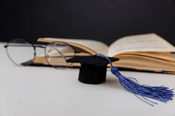 La gorra de graduación y las copas con el libro abierto sobre la mesa. Concéntrate en sombrero — Foto de Stock