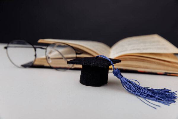 Graduation cap and glasses with open book on a table. Focus on hat