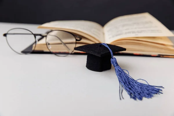 Gorra de graduación y vasos con libro sobre mesa blanca. Concepto de educación y ciencia — Foto de Stock