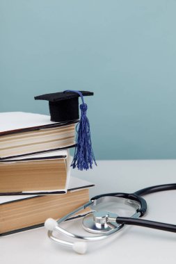 Stetoskop ve mezuniyet şapkası mavi arka planda bir yığın kitap. Tıp eğitimi konsepti. Dikey resim
