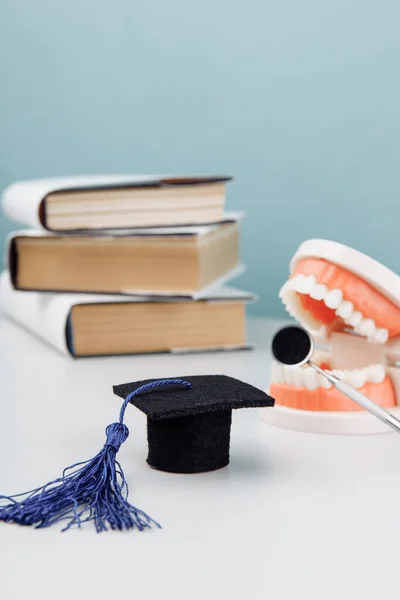 Model of jaw with dentist tool and graduation cap with books. Medical education concept. Vertical image — Stock Photo, Image