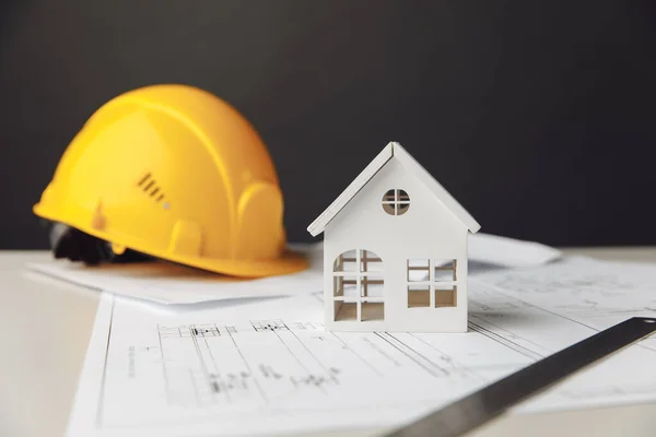 Construction plans with yellow helmet and model of house