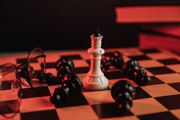 Rey blanco de pie en el tablero de ajedrez alrededor de figuras que caen. Concepto de liderazgo — Foto de Stock