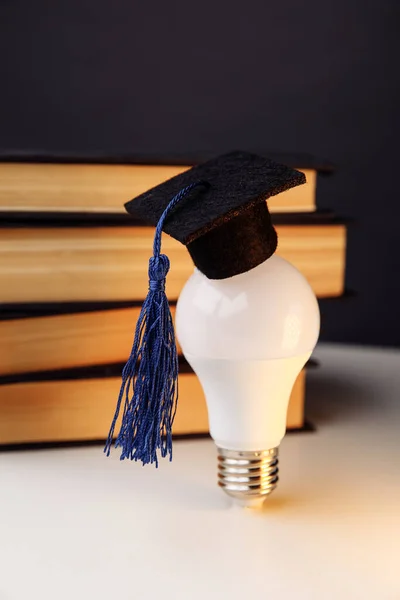 Graduation cap on light bulb with books on a table. Vertical image — Stock Photo, Image