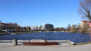 KALININGRAD, RUSYA - 17 Mart 2021: Toprak seti, yaya köprüsü, Crystal House oteli ve ön planda ahşap bir bank..