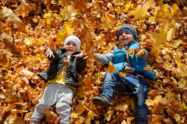 Niños felices en el parque de otoño tumbados sobre hojas —  Fotos de Stock