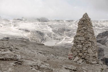 Dolomitlerdeki Sass Pordoi 'nin Yol İşareti rolünde Big Cairn. Bulutlar ve Kar Arkaplandaki Dağı kapladı