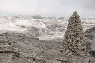 Big Cairn as Path Sign on Sass Pordoi in the Dolomites. Clouds and Snow covered Mountain in the Background clipart