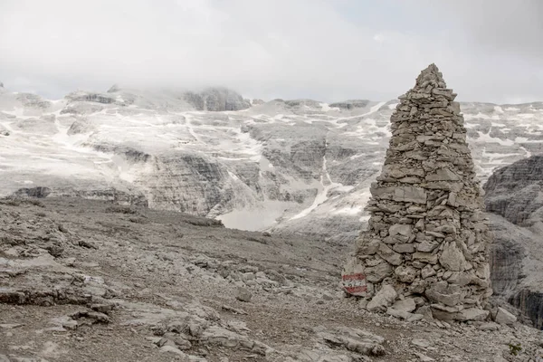 Dolomitlerdeki Sass Pordoi 'nin Yol İşareti rolünde Big Cairn. Bulutlar ve Kar Arkaplandaki Dağı kapladı
