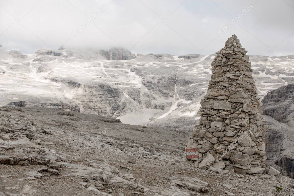 Big Cairn as Path Sign on Sass Pordoi in the Dolomites. Clouds and Snow covered Mountain in the Background