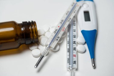 İtalyan yazısıyla analog klinik termometre ve beyaz yüzeyde haplar ve ilaçlarla dijital termometre.
