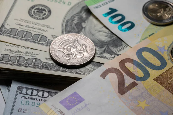 Euros and Dollar currency, one hundred Dollar bills with one hundred and two hundred Euro banknote on top.  Half Dollar coin in focus