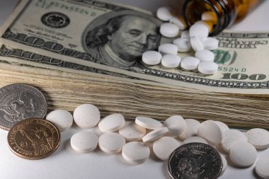 İlaçlar ve ilaçlar odak noktasında, tabletlerin arkasında yığınla para. Yarım Dolar ve Dolar bozuklukları. İlaç giderleri