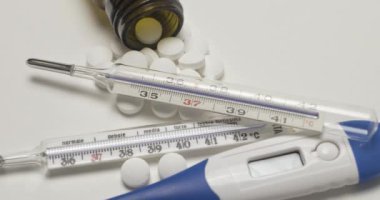 Birden fazla klinik, beyaz yüzeyde ateş termometresi ve beyaz haplar 4K.