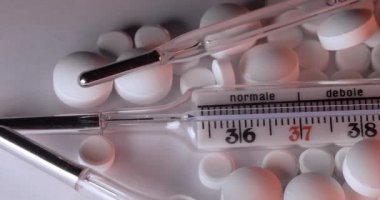 Düşük sıcaklıktan yüksek ateşe kadar İtalyanca yazılar ve selsiyus sıcaklığında cıvalı cam termometre. Farklı haplarla çevrili klinik termometre
