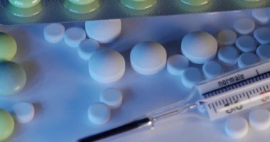 Klinik termometre ve farklı haplar. Antibiyotiklerle çevrili cıva cam termometrede kayma hareketi. Beyaz zemin üzerinde mavi ve beyaz ışık ile termometre