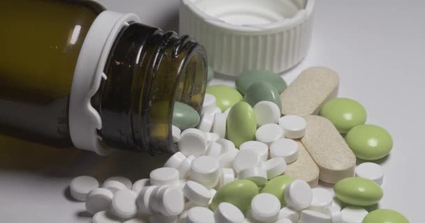 在一个有瓶盖的玻璃瓶中 用不同大小和颜色的药丸进行麻醉 白色表面的药丸和药片 不同形式的抗生素和止痛剂 — 图库视频影像