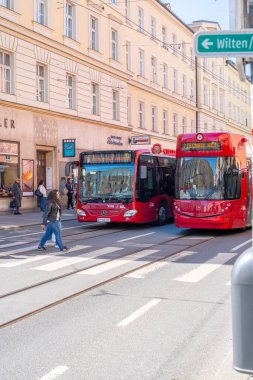 Innsbruck, Avusturya - 20 Mart 2019: Otobüs ve tramvay yan yana bekliyor. Kırmızı Işık Durağı. Yoldan geçen insanlar. Kırmızı otobüs ve tramvay. Avusturya 'da Toplu Taşıma