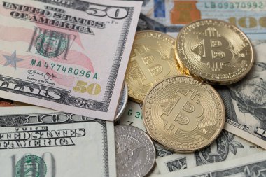 Bitcoin next to fifty and one hundred dollar banknotes. US dollar and crypto currency Bitcoin compared. Digital money with paper money concept