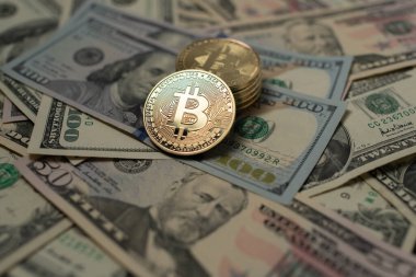 Bitcoin on top of one hundred dollar banknotes. Piled up BTC and spread out dollar bills. Trading cryptocurrency with US dollar.