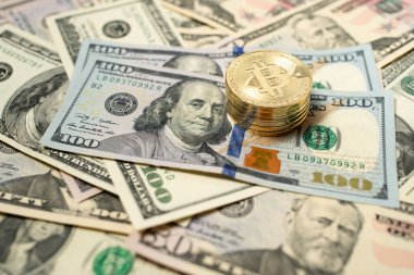Bitcoin dolar banknotlarının üzerine yığılmış. 100 dolarlık banknotların üstüne altın sikkeler. Banknotları arkaplan olarak yay.