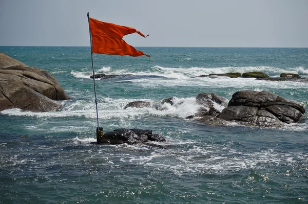 Mar e pedras, bandeira vermelha a tremer ao vento . — Fotografia de Stock
