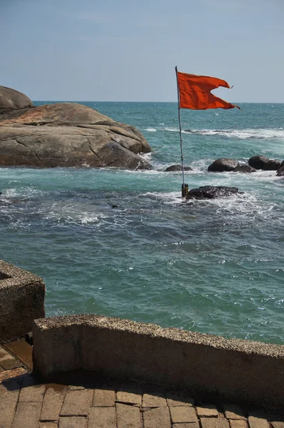 Zee en stenen, rode vlag wapperen in de wind. — Stockfoto