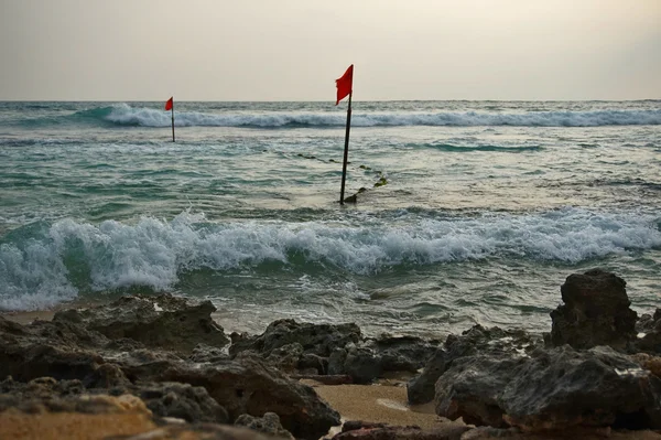 Deniz ve taşlar, kırmızı bayrak rüzgarda çırpınan.