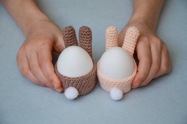 Paskalya tatili hazırlığı. Paskalya tavşanı şeklinde örülmüş yumurta sepeti. Çocuklar yumurta standını tavşan şeklinde tutarlar. Sarı arka plan. Beyaz yumurta. Kartpostal Kendi ellerinle.