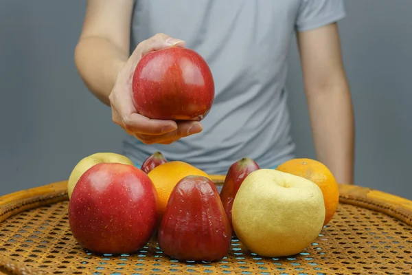 Male holding the apple in one hand and show everyone above a wide variety of fruits are on the table