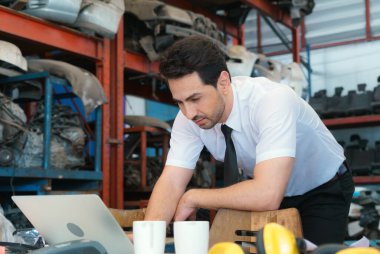 Kafkasyalı işletme müdürü, fabrika deposunda dizüstü bilgisayarla ciddi bir şekilde çalışmaya hazır.