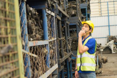 Erkekler birlikte çalışıyor, Asyalı mühendis oto parçasına bakıyor ve fabrika deposunda telsiz kullanıyor.