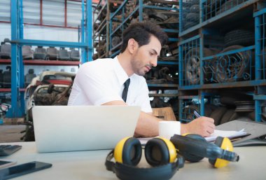 Kafkas işletme müdürü fabrika deposunda dizüstü bilgisayarın önünde oturup rapor yazıyor.