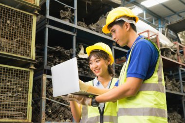 Erkek ve kadın birlikte çalışıyor, Asyalı mühendis çeşitliliği duruyor, gülüyor ve fabrika deposunda dizüstü bilgisayar kullanıyor.