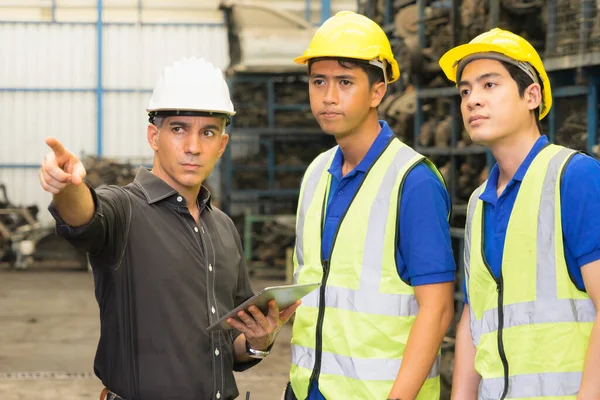 Men and woman work together, diversity of Caucasian manager point at auto part and Asian engineer workers looking at that in factory-warehouse