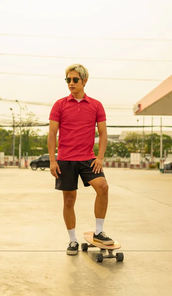 Asian handsome man surf skate or skateboard in summer holiday. Young man stand on skateboard at skateboard way in daylight time.