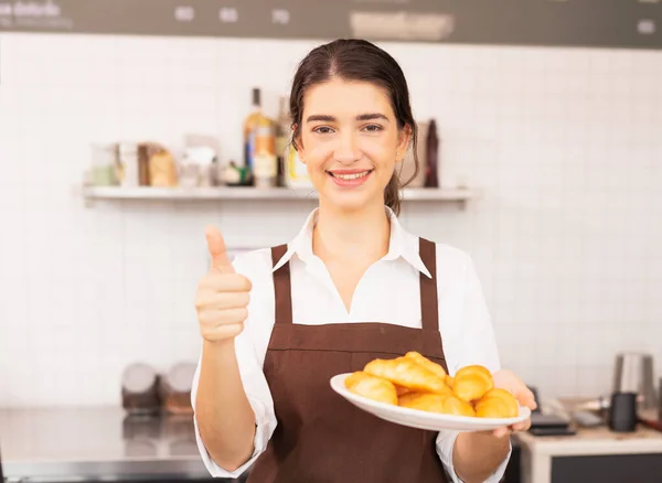 Kafkasyalı güzel kadın elinde ekmekle tabağı tutuyor ve kahve barında baş parmağını bırakıyor. Barista yemek ve kahve servisi işinde çalışıyor..