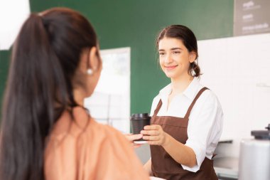 Left side view of beautiful caucasian barista woman happy to give takeaway coffee cup to customer and customer receiving coffee cup. Barista work at coffee bar and food service business