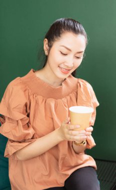 Vertical frame of right side of beautiful Asian woman customer sitting in a happy mood while drinking coffee in coffee bar. Barista work at coffee bar and food service business