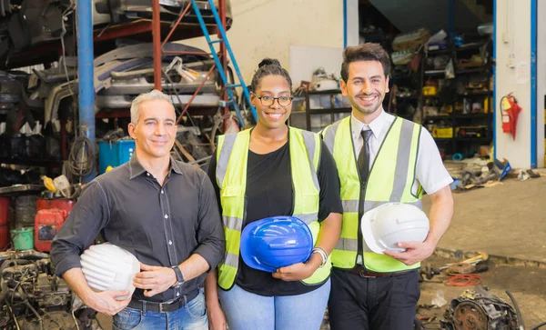 Men and woman work together, holding helmets and looking at right side. Caucasian engineer men and black woman holding helmets in factory-warehouse